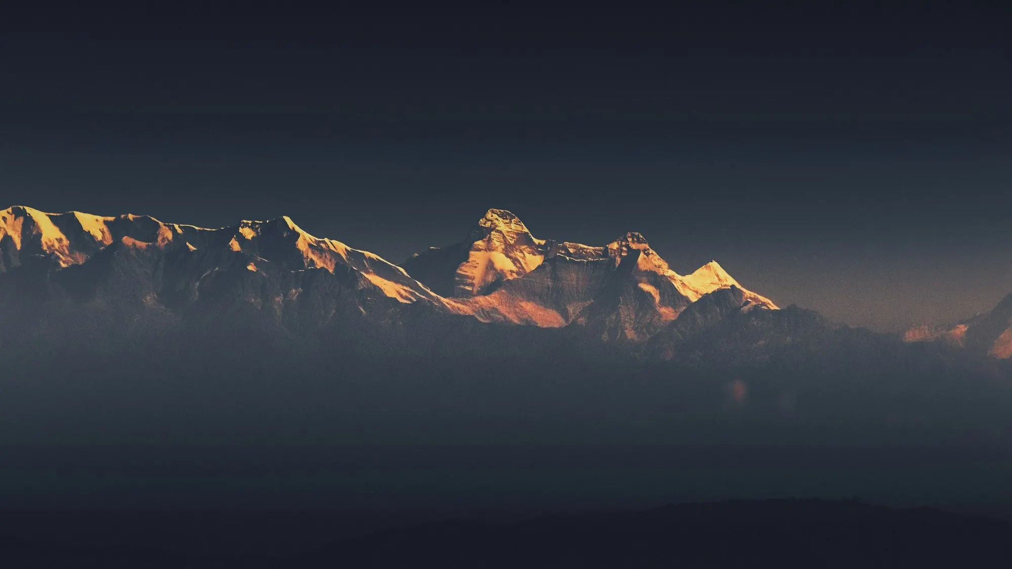 Mountain peaks catching golden first light against a dark sky